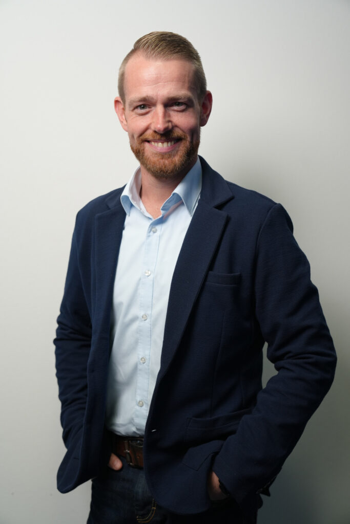 Björn Henk von Haas Paletten lächelt in die Kamera. Mit blondem Bart trägt ein dunkelblaues Sakko und helles Hemd